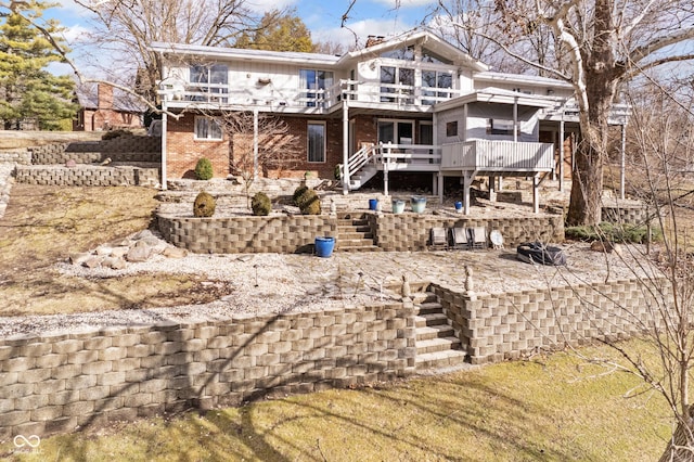 rear view of property featuring a chimney, a balcony, brick siding, stairs, and a patio area