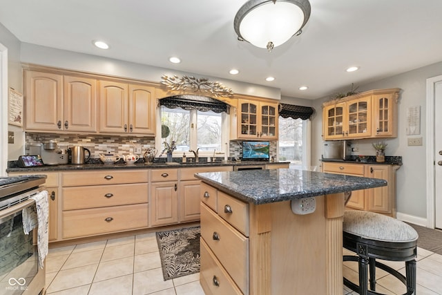 kitchen featuring glass insert cabinets, stainless steel range, light brown cabinets, and a center island