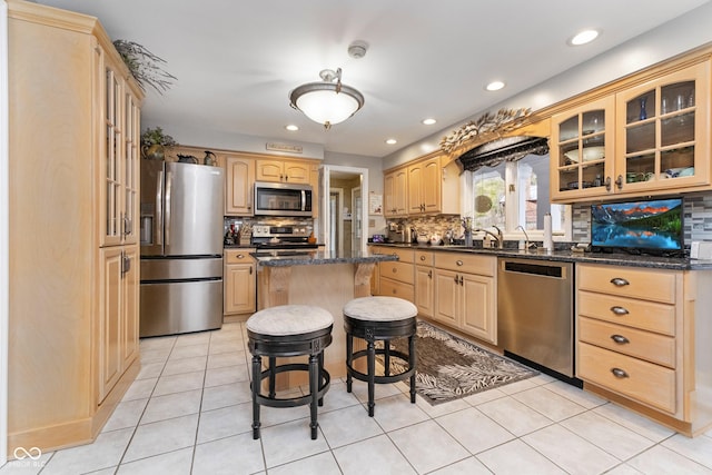 kitchen featuring light brown cabinetry, a center island, stainless steel appliances, and glass insert cabinets