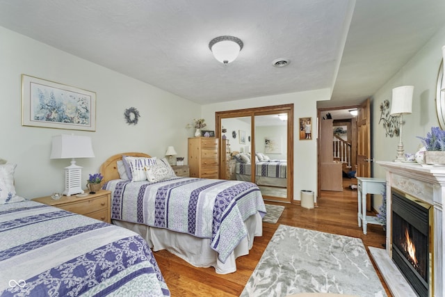 bedroom with a closet, a fireplace with flush hearth, visible vents, and wood finished floors