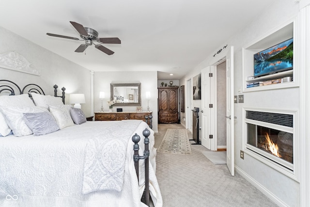 bedroom with a glass covered fireplace, ceiling fan, baseboards, and light carpet