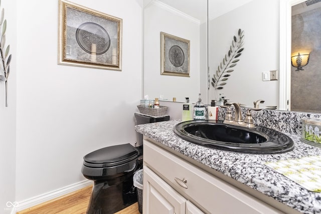 half bathroom featuring toilet, ornamental molding, wood finished floors, baseboards, and vanity