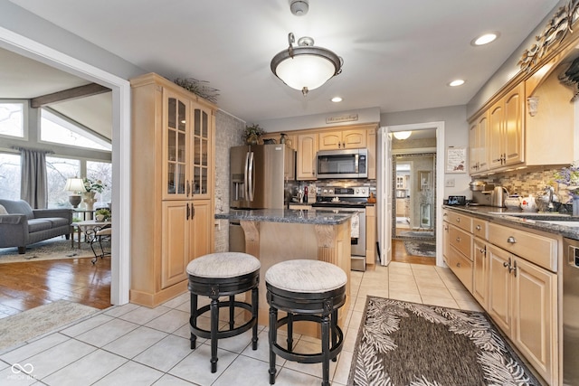 kitchen with a kitchen island, glass insert cabinets, light brown cabinetry, a kitchen bar, and stainless steel appliances