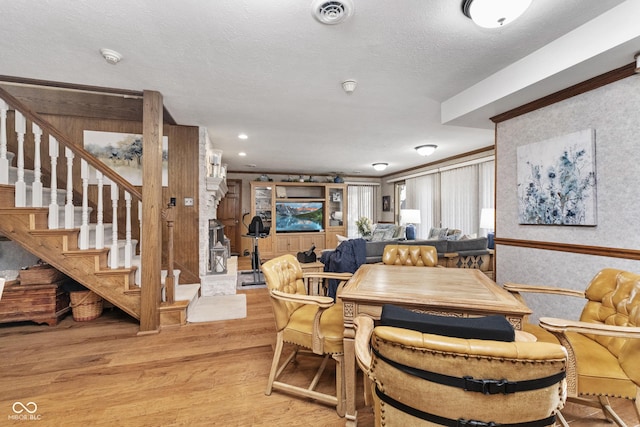 dining area with visible vents, wallpapered walls, light wood-style flooring, stairs, and a textured ceiling