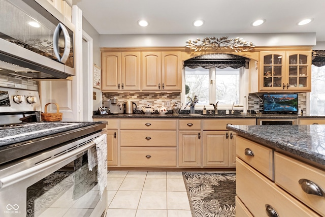 kitchen featuring light brown cabinets, glass insert cabinets, light tile patterned floors, stainless steel appliances, and a sink