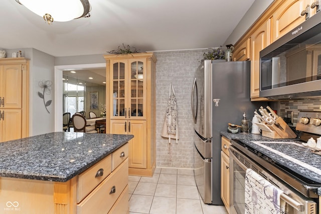 kitchen with light tile patterned floors, a kitchen island, light brown cabinetry, stainless steel appliances, and glass insert cabinets