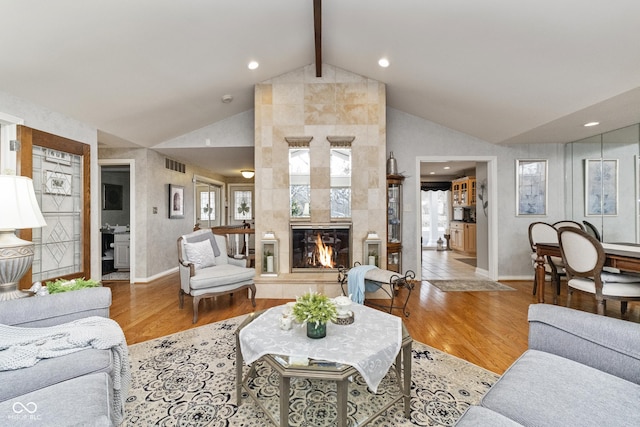 living area with visible vents, beam ceiling, a tiled fireplace, wood finished floors, and baseboards