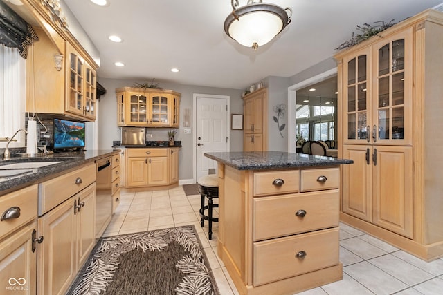 kitchen featuring a breakfast bar, light brown cabinets, a sink, stainless steel dishwasher, and light tile patterned floors