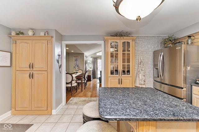 kitchen featuring light brown cabinetry, a breakfast bar, light tile patterned flooring, and stainless steel refrigerator with ice dispenser