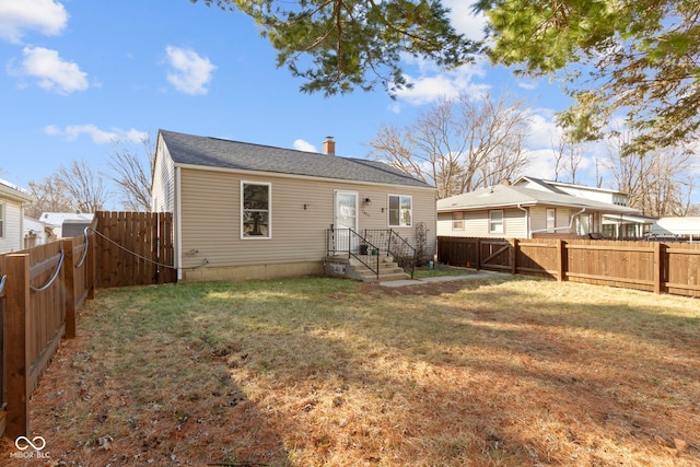 back of property with a lawn, a chimney, and a fenced backyard