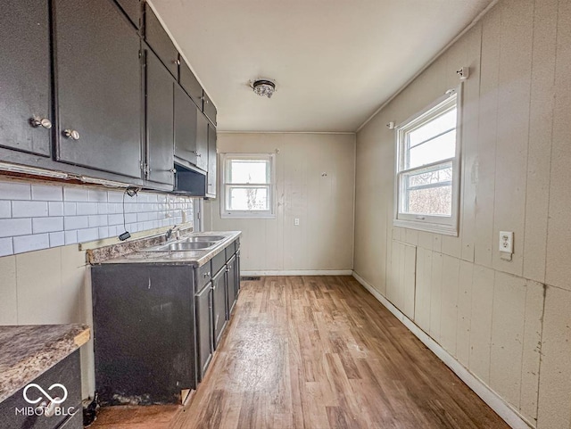 kitchen featuring wooden walls, baseboards, light countertops, light wood-type flooring, and a sink