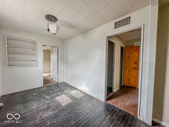 unfurnished room featuring built in shelves, visible vents, and wood finished floors