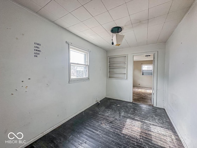 empty room featuring built in shelves, a wealth of natural light, baseboards, and wood finished floors