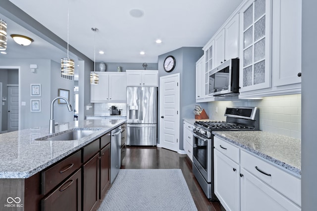 kitchen with a sink, dark brown cabinets, dark wood-style floors, stainless steel appliances, and a kitchen island with sink