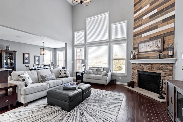 living area featuring a notable chandelier, a fireplace, dark wood-style flooring, and a towering ceiling