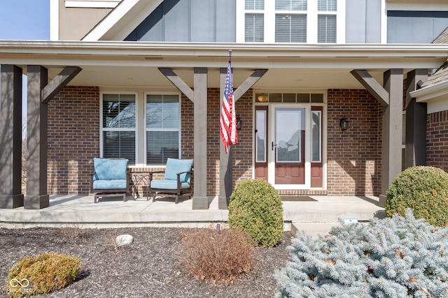 view of exterior entry with brick siding, covered porch, and board and batten siding