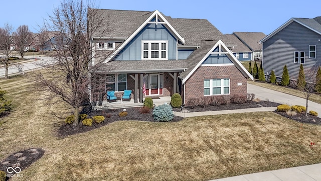 view of front facade featuring roof with shingles, a porch, brick siding, a front lawn, and board and batten siding