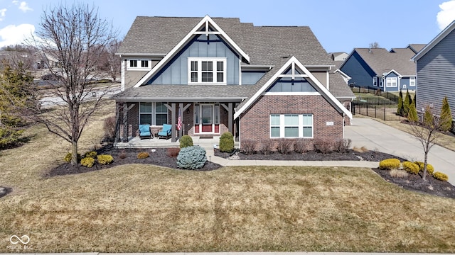 view of front of home featuring a front lawn, a porch, board and batten siding, a shingled roof, and brick siding