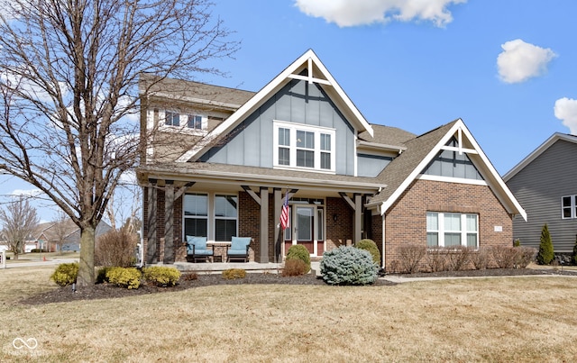 view of front of property featuring brick siding, board and batten siding, a shingled roof, a front lawn, and covered porch