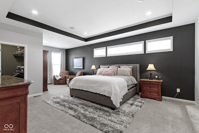 bedroom with a tray ceiling, multiple windows, and light colored carpet