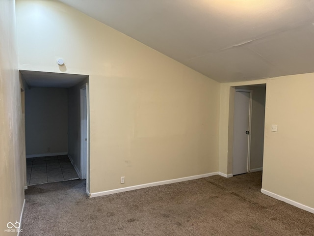 carpeted spare room featuring vaulted ceiling and baseboards