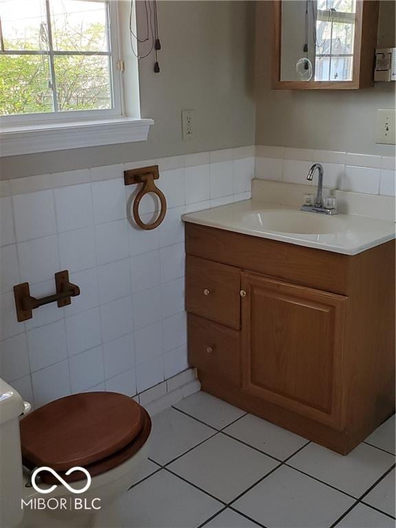 bathroom with toilet, a wainscoted wall, tile patterned floors, vanity, and tile walls