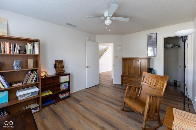 sitting room featuring a ceiling fan, wood finished floors, visible vents, and a textured ceiling