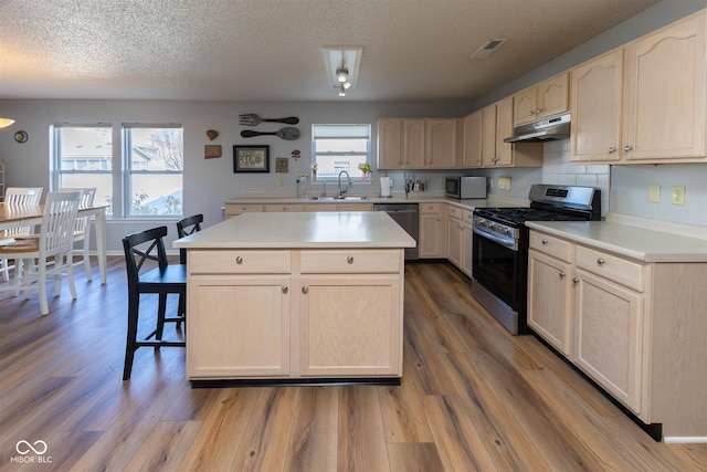 kitchen featuring light brown cabinets, under cabinet range hood, light countertops, stainless steel appliances, and a sink