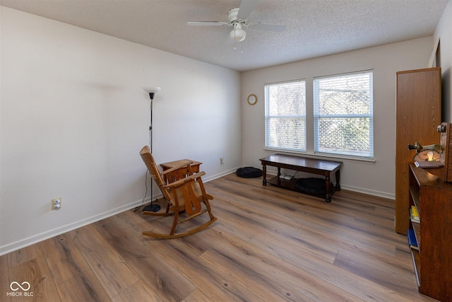 living area with baseboards, a textured ceiling, light wood-style flooring, and a ceiling fan