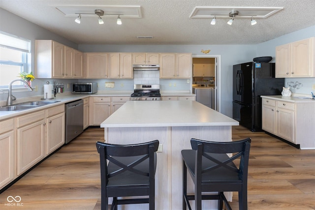 kitchen featuring wood finished floors, a sink, stainless steel appliances, under cabinet range hood, and washer and dryer