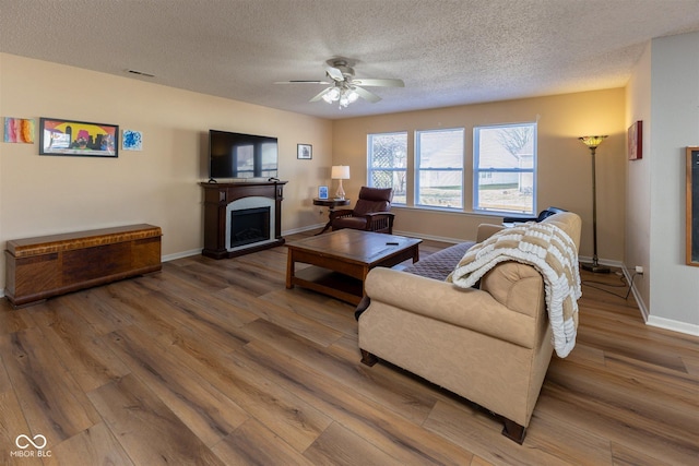 living area with a fireplace, baseboards, a ceiling fan, and wood finished floors