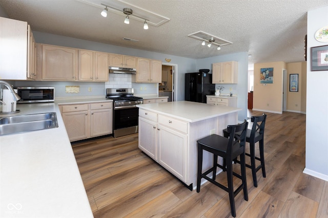 kitchen with under cabinet range hood, freestanding refrigerator, wood finished floors, stainless steel gas range, and a sink