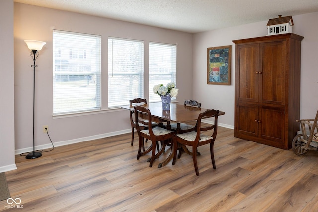 dining area featuring light wood-style flooring, baseboards, and a textured ceiling