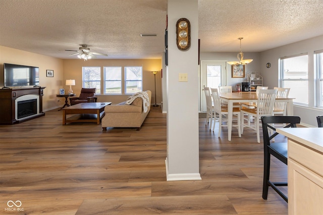 living area with visible vents, a ceiling fan, a textured ceiling, light wood-style floors, and a fireplace