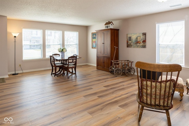 living area with visible vents, a textured ceiling, light wood-type flooring, and baseboards