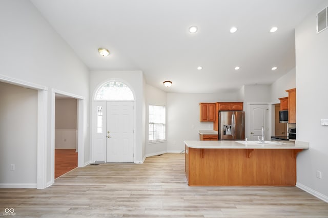 kitchen with a sink, stainless steel appliances, a peninsula, light wood finished floors, and light countertops