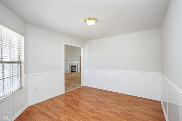 unfurnished room featuring light wood-type flooring, a wainscoted wall, and a tiled fireplace