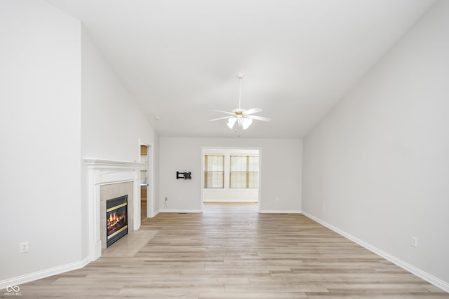 unfurnished living room with lofted ceiling, a fireplace, light wood finished floors, baseboards, and ceiling fan