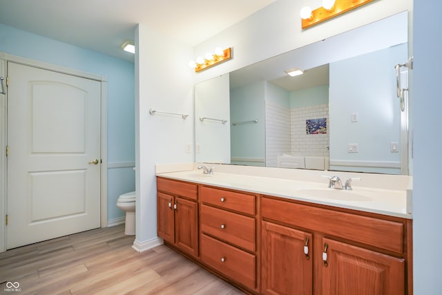 bathroom with toilet, double vanity, a sink, wood finished floors, and a shower