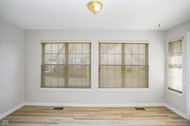 unfurnished room with a wealth of natural light, visible vents, and wood finished floors