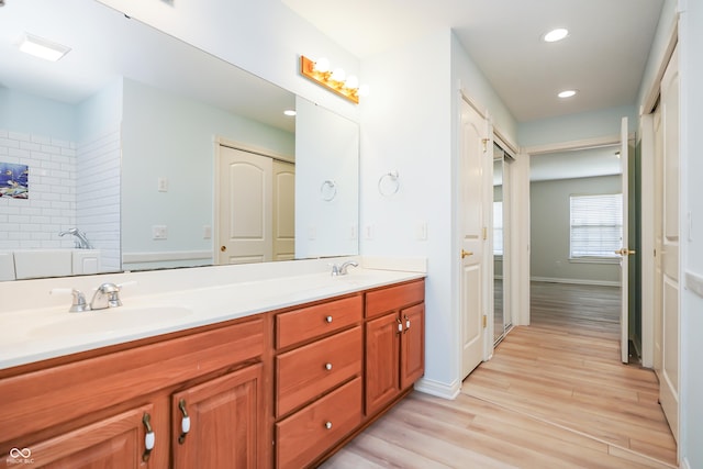 bathroom with wood finished floors, baseboards, double vanity, recessed lighting, and a sink