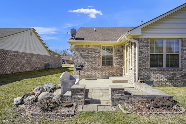 back of house featuring brick siding, a patio area, a lawn, and roof with shingles