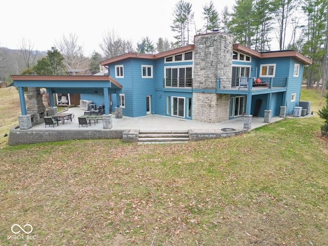 rear view of property with stone siding, a patio, a chimney, and a lawn