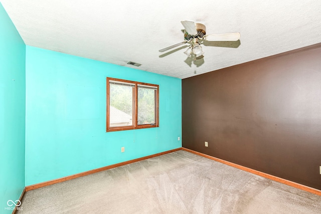 unfurnished room with a textured ceiling, carpet floors, a ceiling fan, visible vents, and baseboards