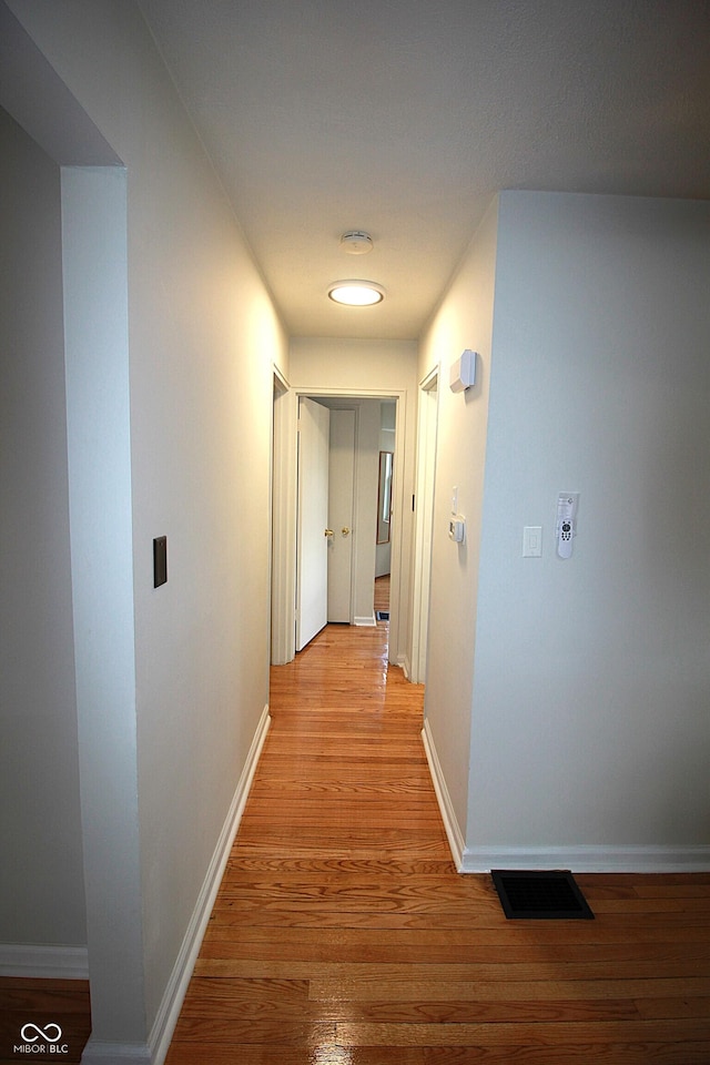 hallway with light wood-type flooring, baseboards, and visible vents