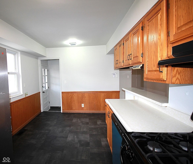 kitchen with brown cabinetry, wainscoting, black gas stove, and wooden walls