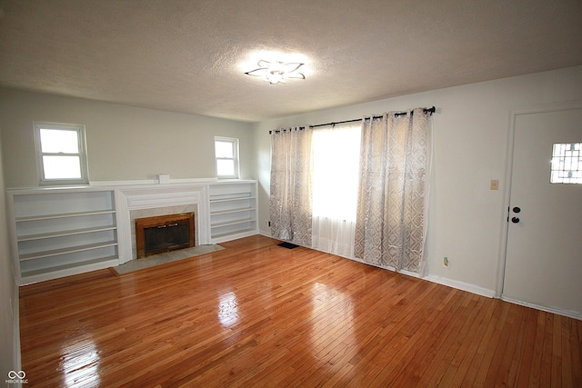 unfurnished living room featuring visible vents, baseboards, wood-type flooring, a textured ceiling, and a high end fireplace