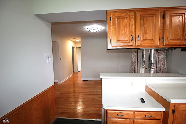 kitchen featuring brown cabinetry, light countertops, wood finished floors, and a wainscoted wall