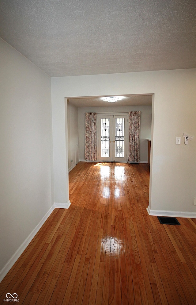 spare room with a textured ceiling, visible vents, baseboards, french doors, and wood-type flooring