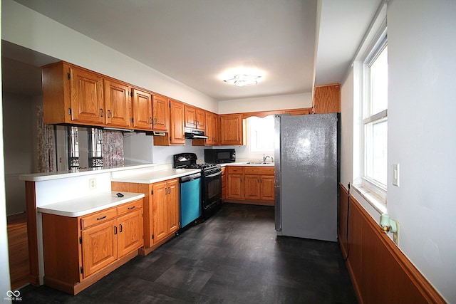 kitchen featuring brown cabinets, light countertops, a peninsula, under cabinet range hood, and black appliances